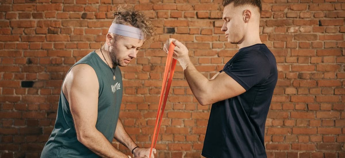 Two men engaging in a resistance band workout in a brick-walled gym setting.