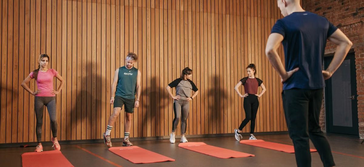A group exercise class with a personal trainer leading stretching exercises in a gym.