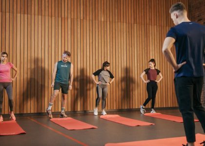 A group exercise class with a personal trainer leading stretching exercises in a gym.